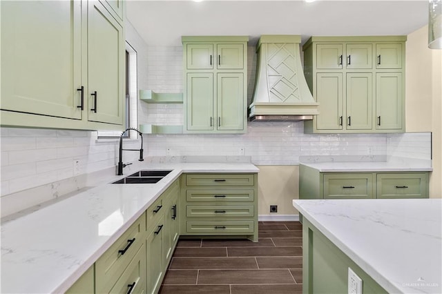 kitchen featuring premium range hood, green cabinets, light stone counters, and sink