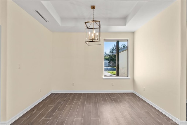 empty room with a tray ceiling, dark hardwood / wood-style floors, and a notable chandelier