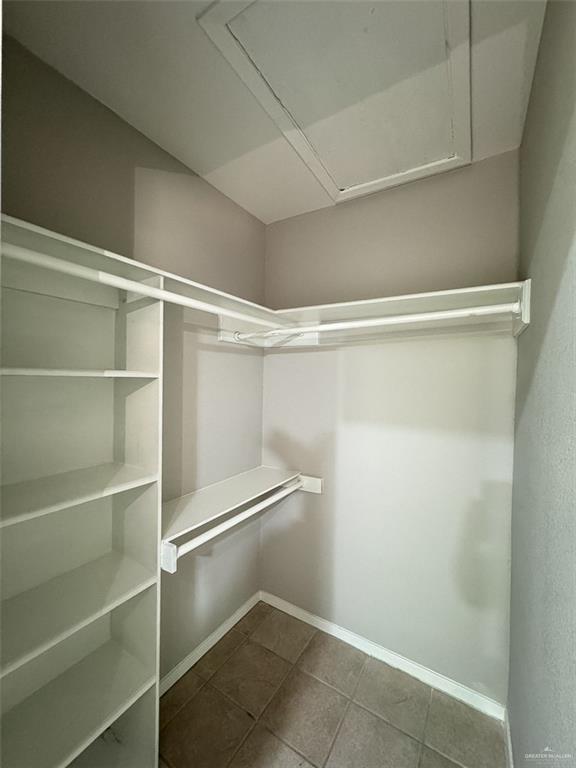 spacious closet featuring attic access and dark tile patterned floors