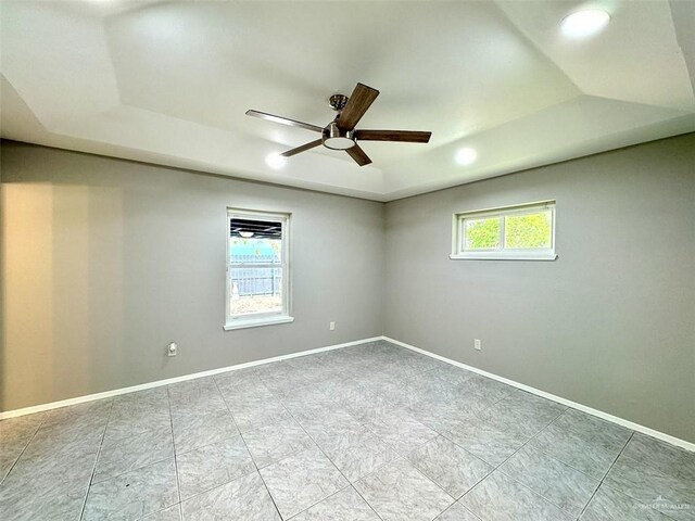 tiled spare room with a ceiling fan, baseboards, and a tray ceiling