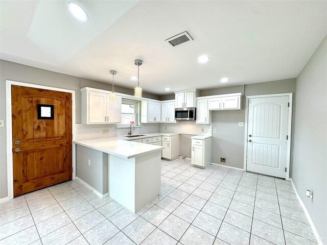 kitchen with stainless steel microwave, a sink, light tile patterned flooring, a peninsula, and white cabinets