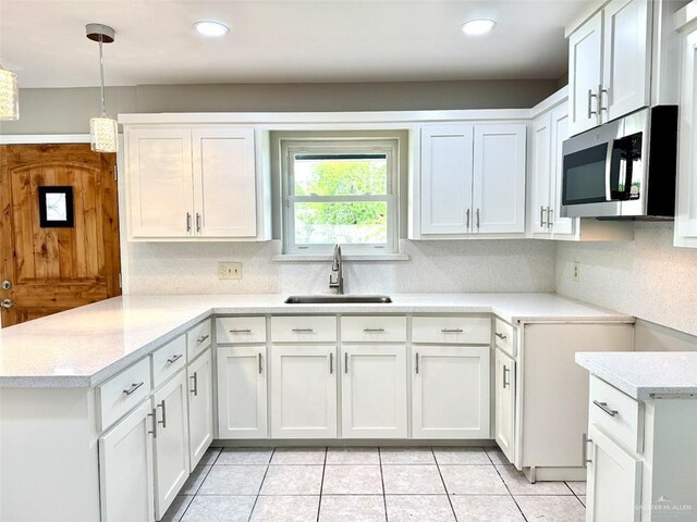 kitchen featuring stainless steel microwave, light countertops, a sink, white cabinetry, and a peninsula
