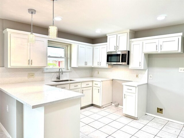 kitchen featuring stainless steel microwave, a sink, decorative light fixtures, backsplash, and a peninsula