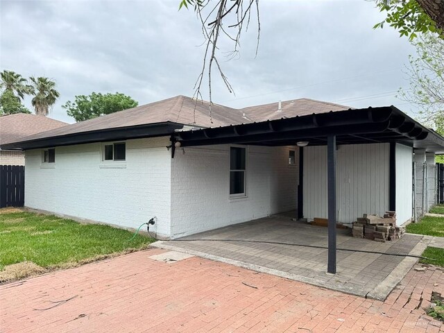 rear view of property featuring fence, roof with shingles, a carport, and brick siding