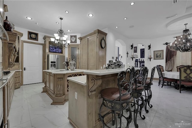 kitchen featuring gas cooktop, a kitchen breakfast bar, stainless steel fridge, an island with sink, and decorative light fixtures