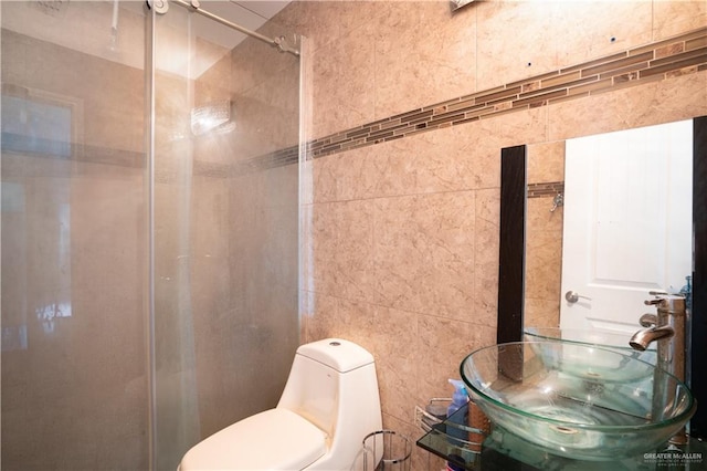 bathroom with tiled shower, toilet, sink, and tile walls