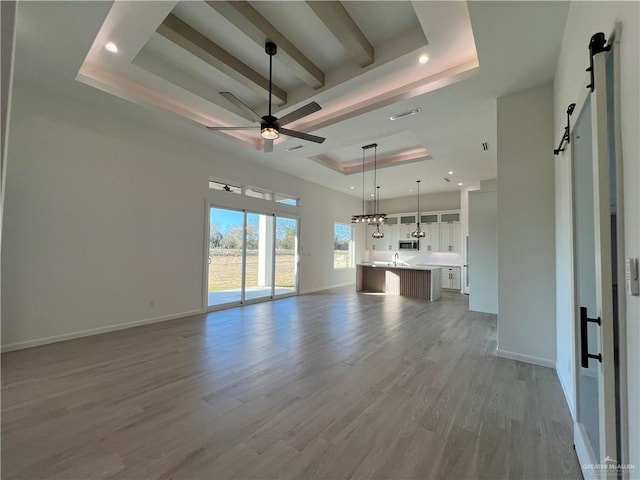 unfurnished living room with sink, a raised ceiling, ceiling fan, a barn door, and hardwood / wood-style floors