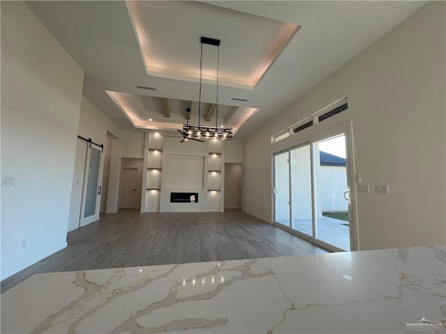 unfurnished living room featuring wood-type flooring, a raised ceiling, ceiling fan, and a barn door