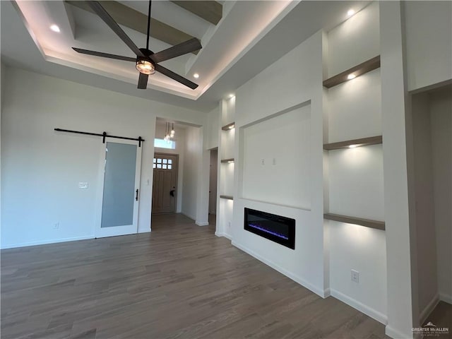 unfurnished living room featuring a raised ceiling, a towering ceiling, hardwood / wood-style flooring, ceiling fan, and a barn door