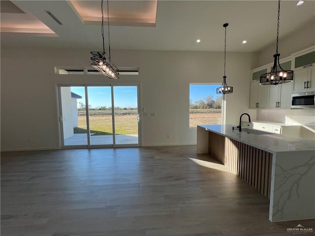 kitchen featuring decorative light fixtures, a tray ceiling, light stone countertops, hardwood / wood-style floors, and white cabinets