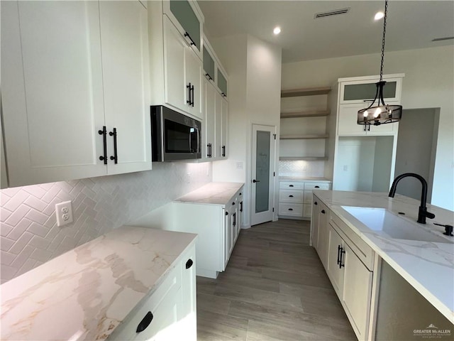 kitchen featuring pendant lighting, sink, light stone counters, and backsplash