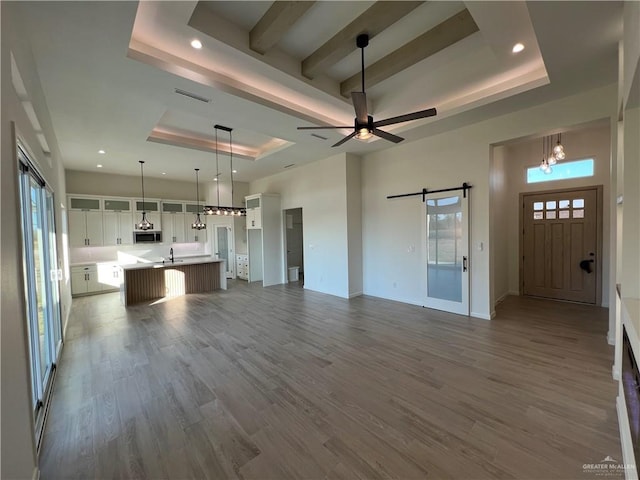 unfurnished living room featuring wood-type flooring, a barn door, sink, and a tray ceiling