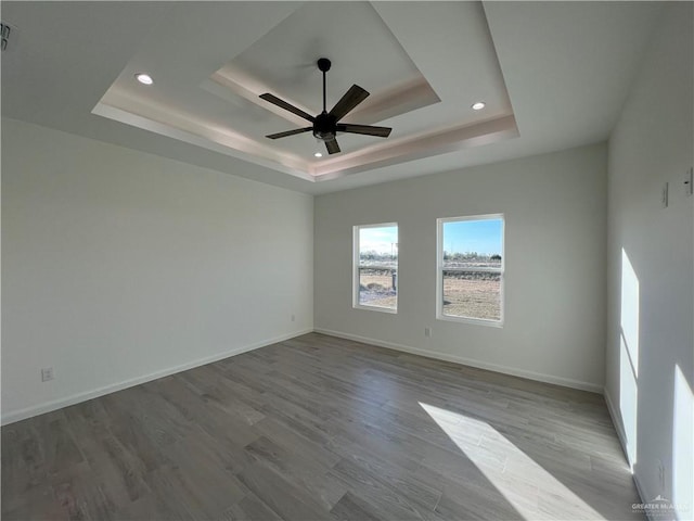 empty room featuring a raised ceiling, ceiling fan, and light wood-type flooring