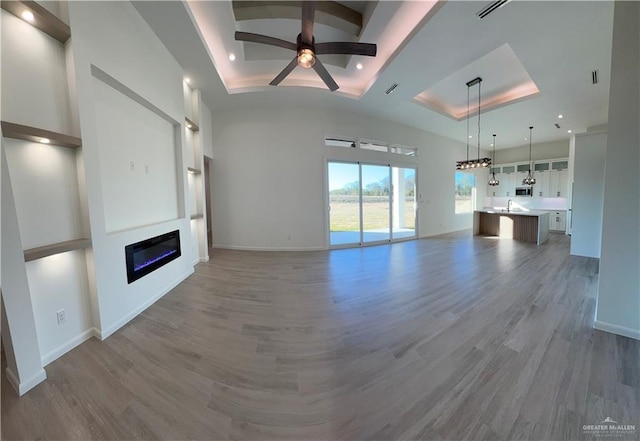 unfurnished living room with ceiling fan, sink, a tray ceiling, and hardwood / wood-style floors