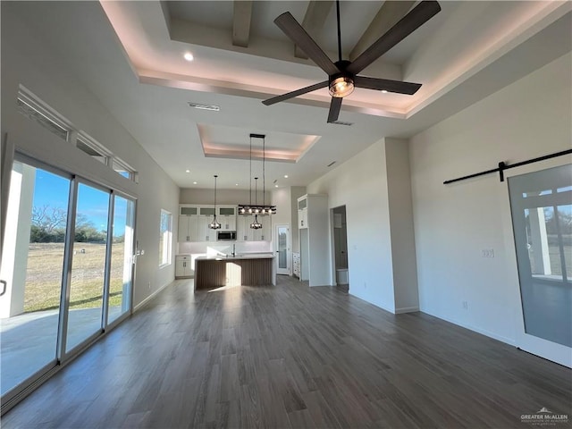 unfurnished living room featuring a tray ceiling, dark wood-type flooring, a barn door, and ceiling fan