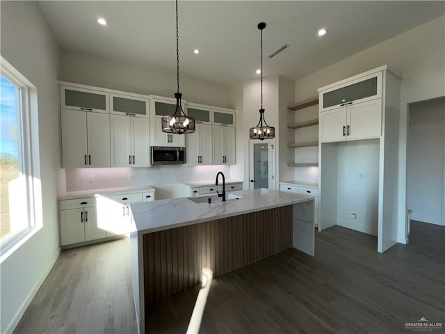 kitchen featuring white cabinetry, sink, light stone counters, and an island with sink