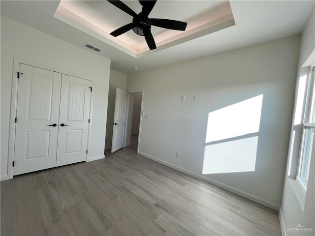 unfurnished bedroom with a tray ceiling, a closet, ceiling fan, and light wood-type flooring