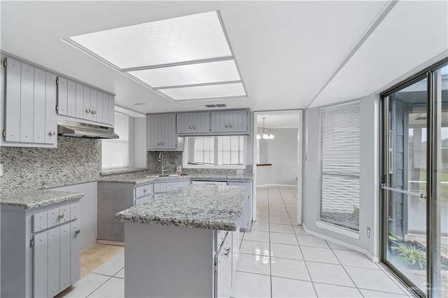 kitchen featuring light tile patterned floors, a center island, gray cabinets, and tasteful backsplash