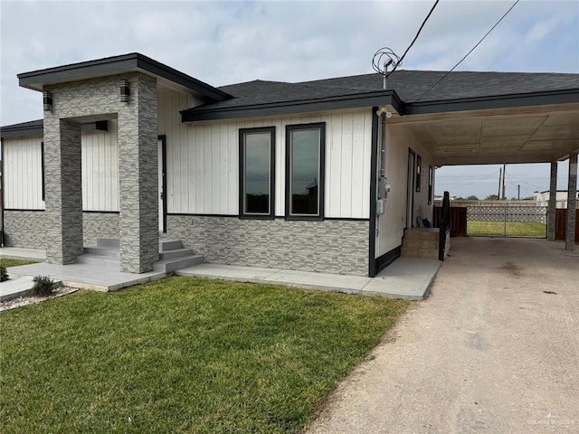 view of front of property featuring entry steps, an attached carport, stone siding, driveway, and a front lawn