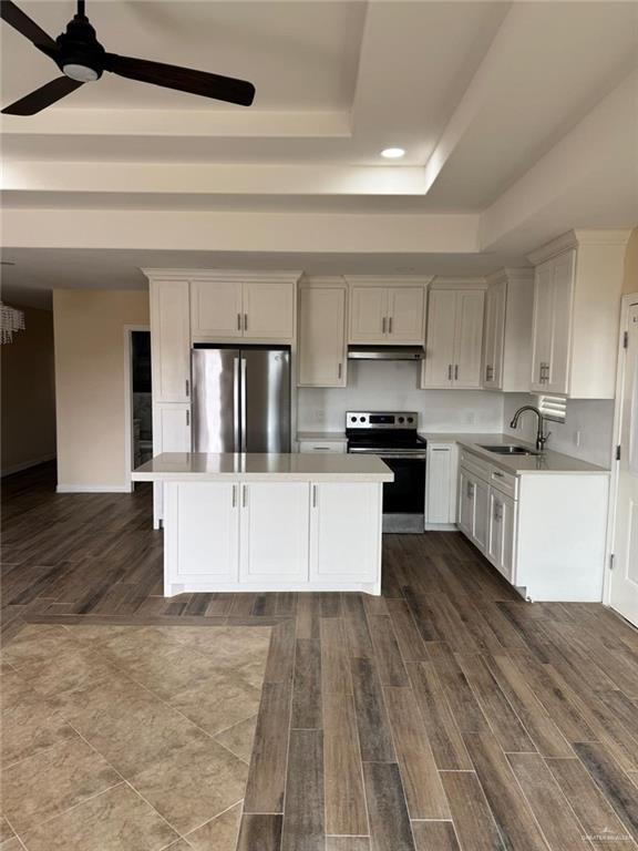 kitchen featuring a raised ceiling, a kitchen island, stainless steel appliances, light countertops, and a sink