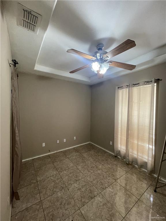 empty room featuring a tray ceiling, ceiling fan, and tile patterned flooring