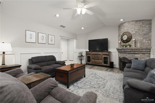 living room with wood finished floors, visible vents, lofted ceiling, wainscoting, and a brick fireplace