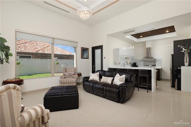 living room with a tray ceiling, an inviting chandelier, a towering ceiling, and visible vents