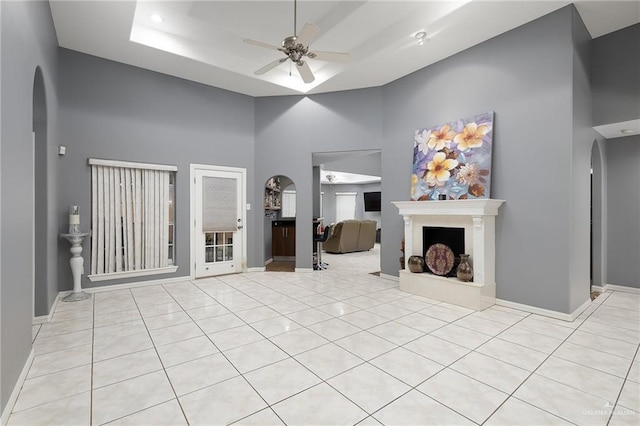 living room featuring a raised ceiling, ceiling fan, and light tile patterned flooring