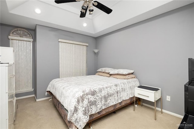 bedroom with ceiling fan, light colored carpet, and a tray ceiling