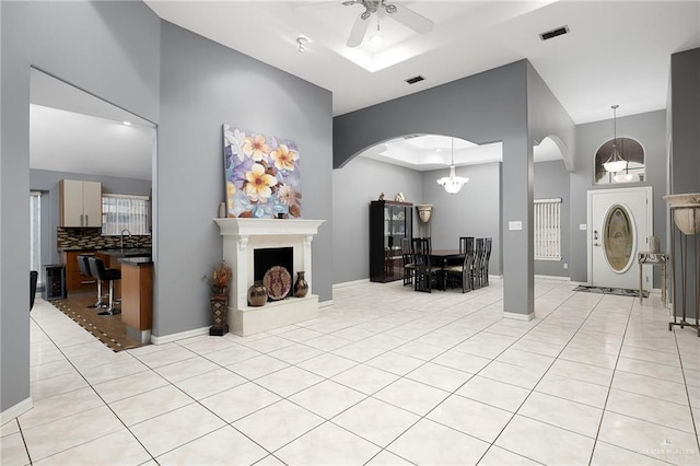 tiled living room with ceiling fan with notable chandelier, a raised ceiling, and sink