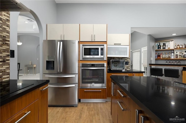 kitchen with backsplash, white cabinetry, light wood-type flooring, and appliances with stainless steel finishes