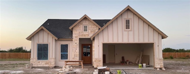 modern farmhouse style home featuring a garage, stone siding, fence, and board and batten siding
