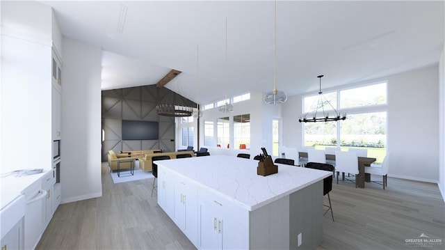 kitchen with light wood-style flooring, white cabinetry, a kitchen island, high vaulted ceiling, and a kitchen bar