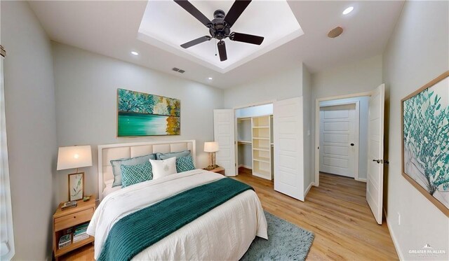 bedroom featuring ceiling fan, a raised ceiling, a spacious closet, a closet, and light wood-type flooring