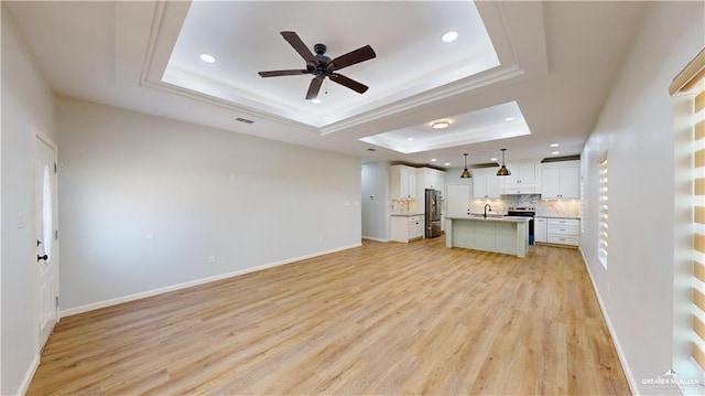 unfurnished living room featuring a raised ceiling, ceiling fan, sink, and light wood-type flooring