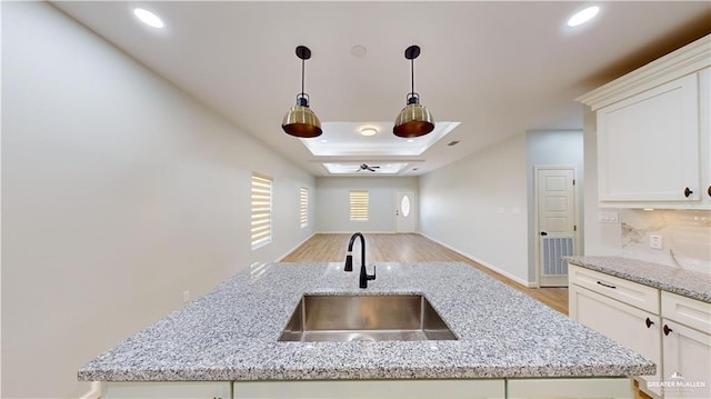 kitchen with tasteful backsplash, sink, white cabinets, light stone counters, and light wood-type flooring