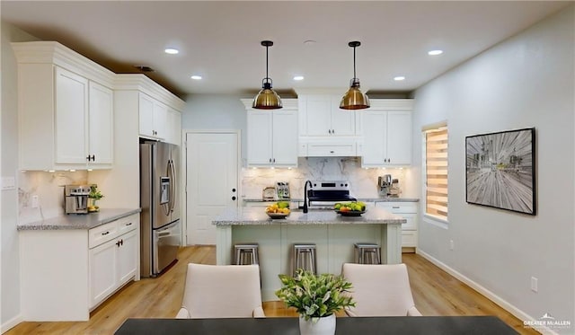 kitchen featuring appliances with stainless steel finishes, pendant lighting, white cabinetry, a kitchen island with sink, and light stone counters