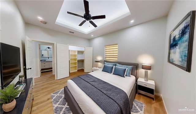 bedroom featuring a raised ceiling, ceiling fan, a spacious closet, and light wood-type flooring