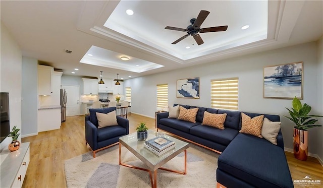 living room with light hardwood / wood-style floors, a raised ceiling, and ceiling fan