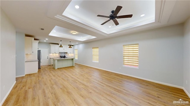 unfurnished living room featuring a raised ceiling, ceiling fan, and light hardwood / wood-style floors