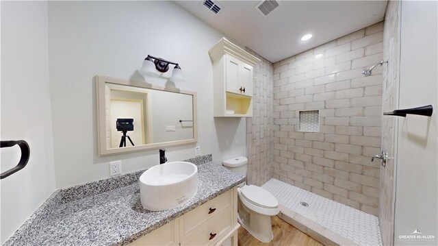 bathroom with hardwood / wood-style flooring, vanity, a tile shower, and toilet