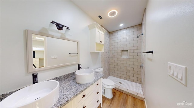 bathroom featuring a tile shower, vanity, hardwood / wood-style flooring, and toilet