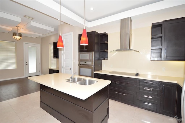 kitchen with stainless steel oven, sink, wall chimney range hood, light hardwood / wood-style floors, and a center island with sink