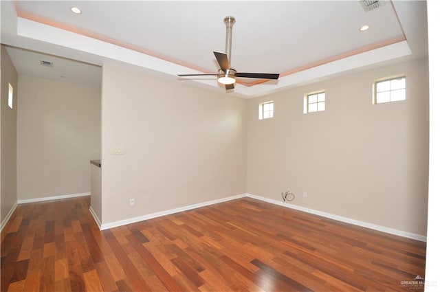 empty room with a tray ceiling, ceiling fan, and dark hardwood / wood-style floors