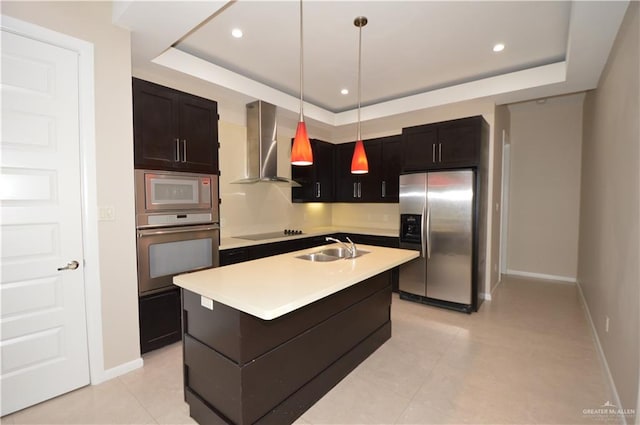 kitchen featuring a center island with sink, wall chimney range hood, hanging light fixtures, sink, and appliances with stainless steel finishes