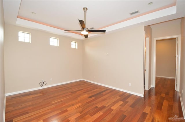 empty room featuring dark hardwood / wood-style flooring, a tray ceiling, and ceiling fan