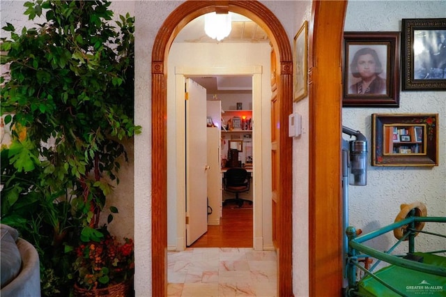 corridor with marble look tiles, arched walkways, and a textured wall