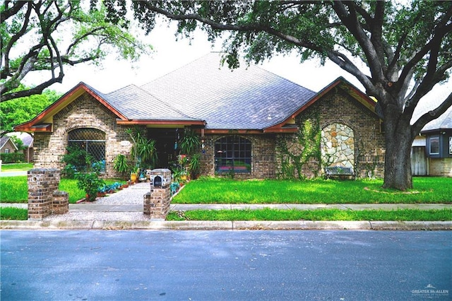 view of front of home with brick siding, roof with shingles, and a front yard