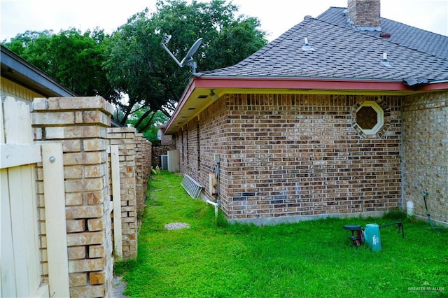 view of side of property with brick siding, roof with shingles, a lawn, and a chimney