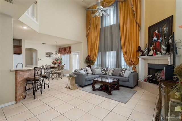 tiled living room featuring ceiling fan with notable chandelier, a high ceiling, a wealth of natural light, and a tiled fireplace